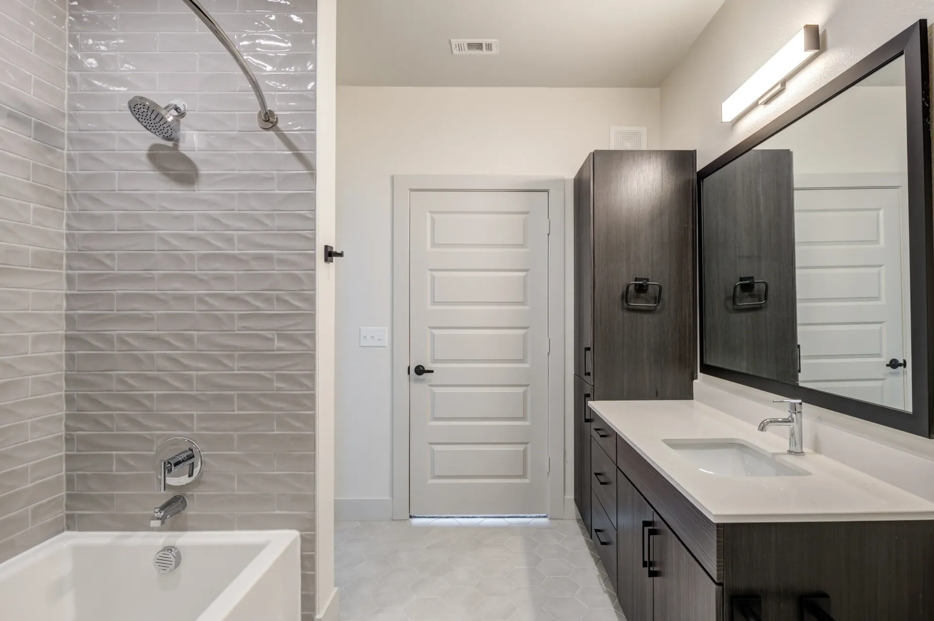 Modern bathroom with white subway tile shower, vanity with white countertop, and dark wood cabinetry.