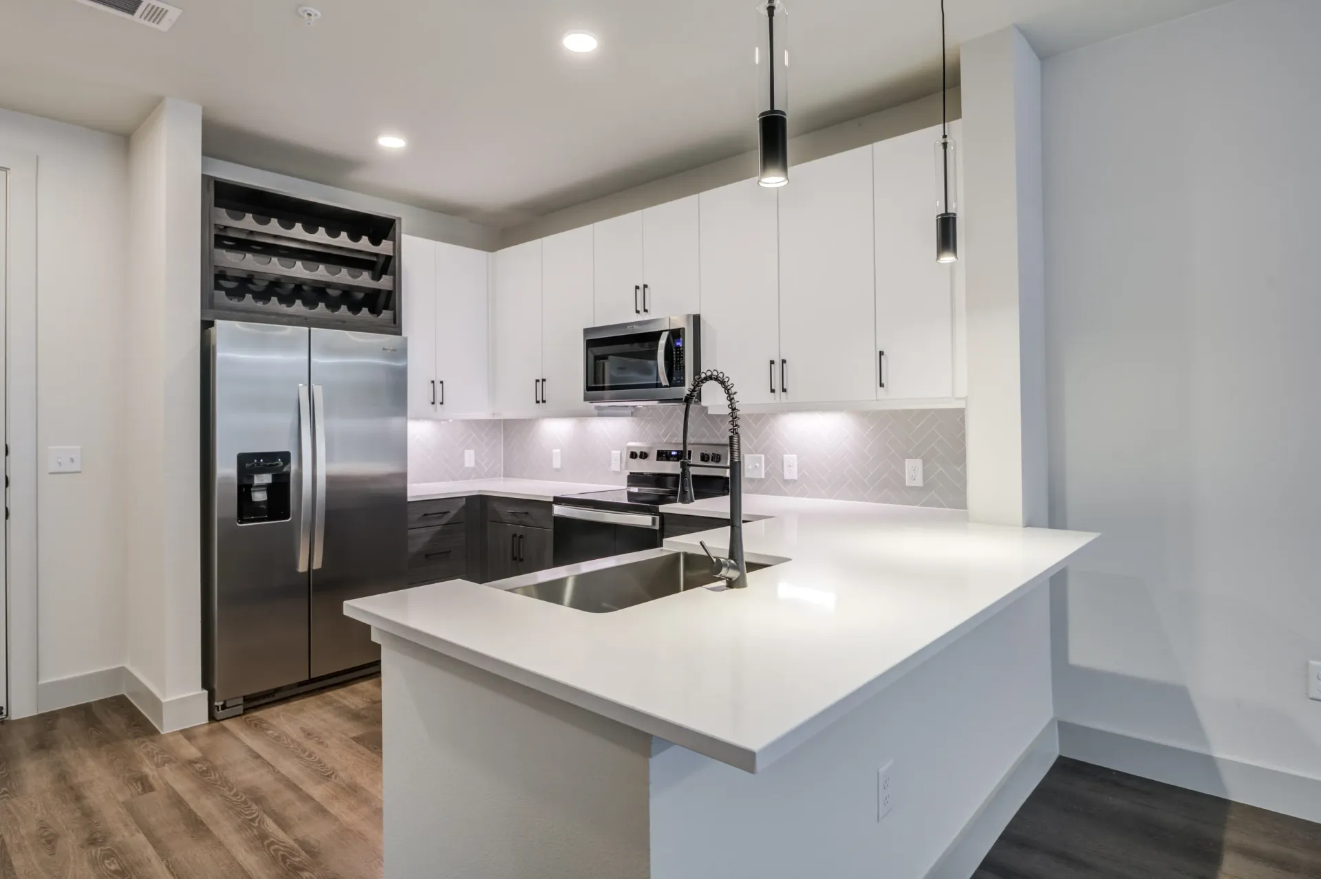 Modern kitchen with stainless steel appliances, white countertops, and dark lower cabinets.