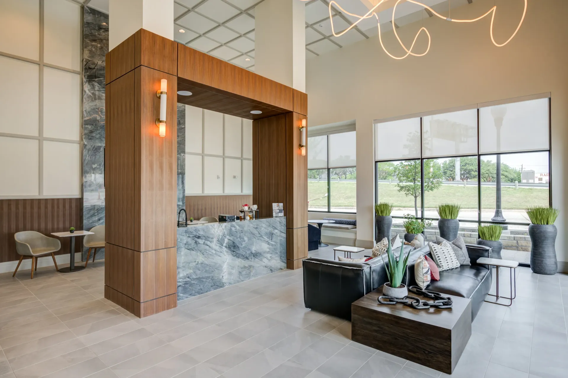 Modern lobby with a marble front desk, comfortable seating, and large windows overlooking an outdoor area.
