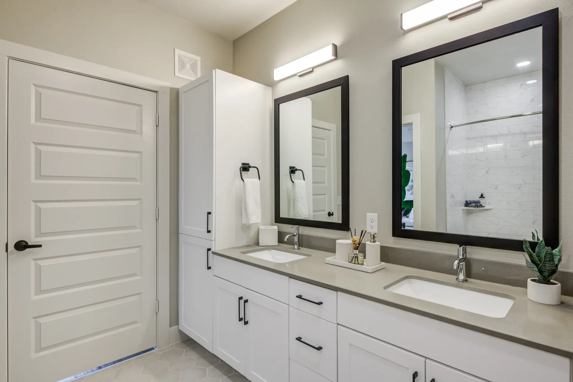 Double vanity with two sinks, mirrors, and ample storage, plus a door and a shower visible in the reflection.