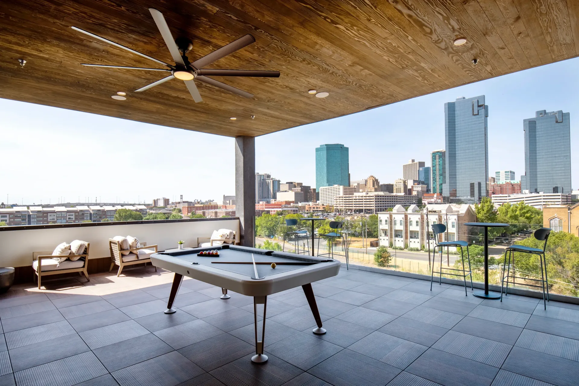 Covered balcony with pool table, seating, and city skyline view.