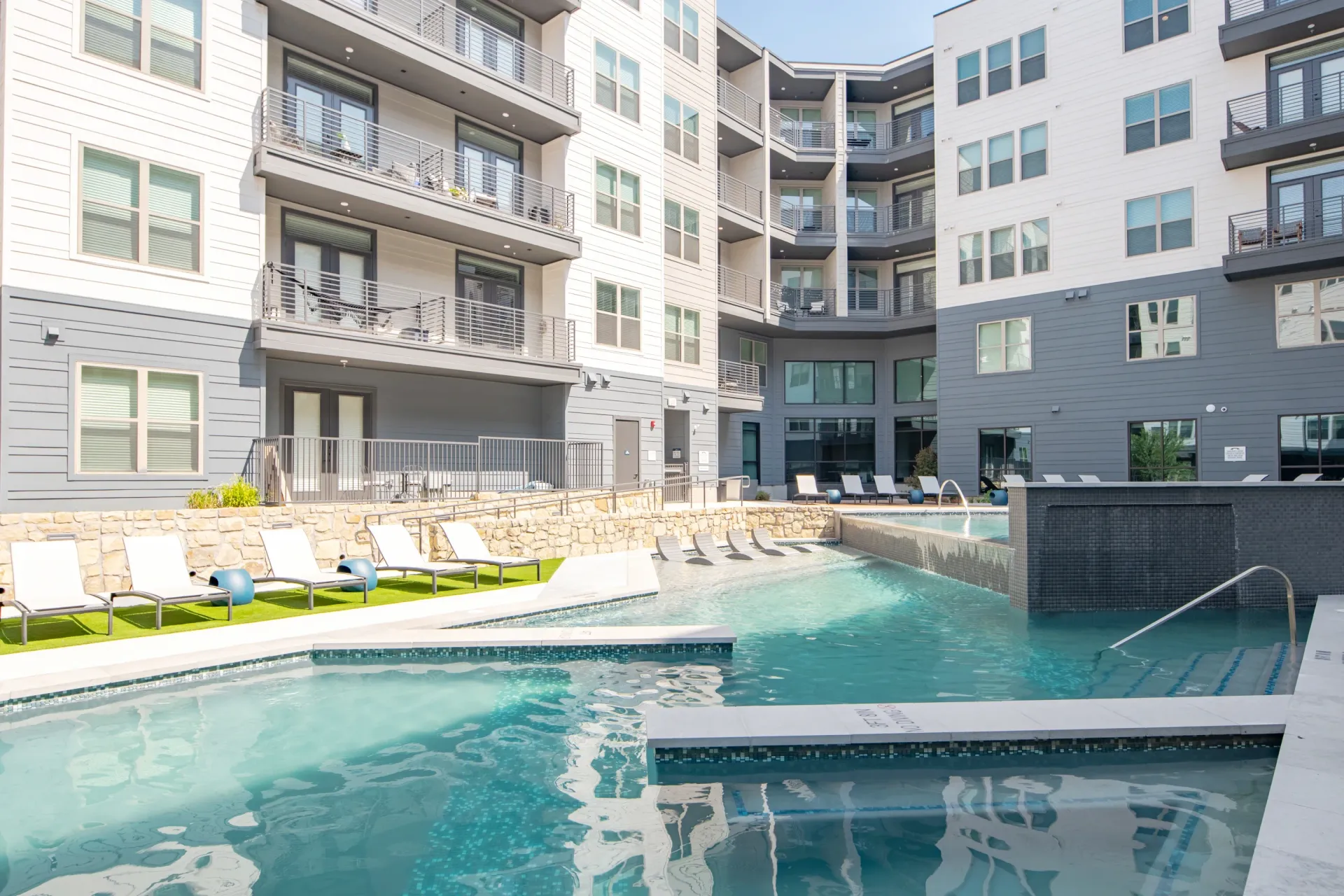 Resort-style swimming pool with lounge chairs and waterfalls at a modern apartment complex.