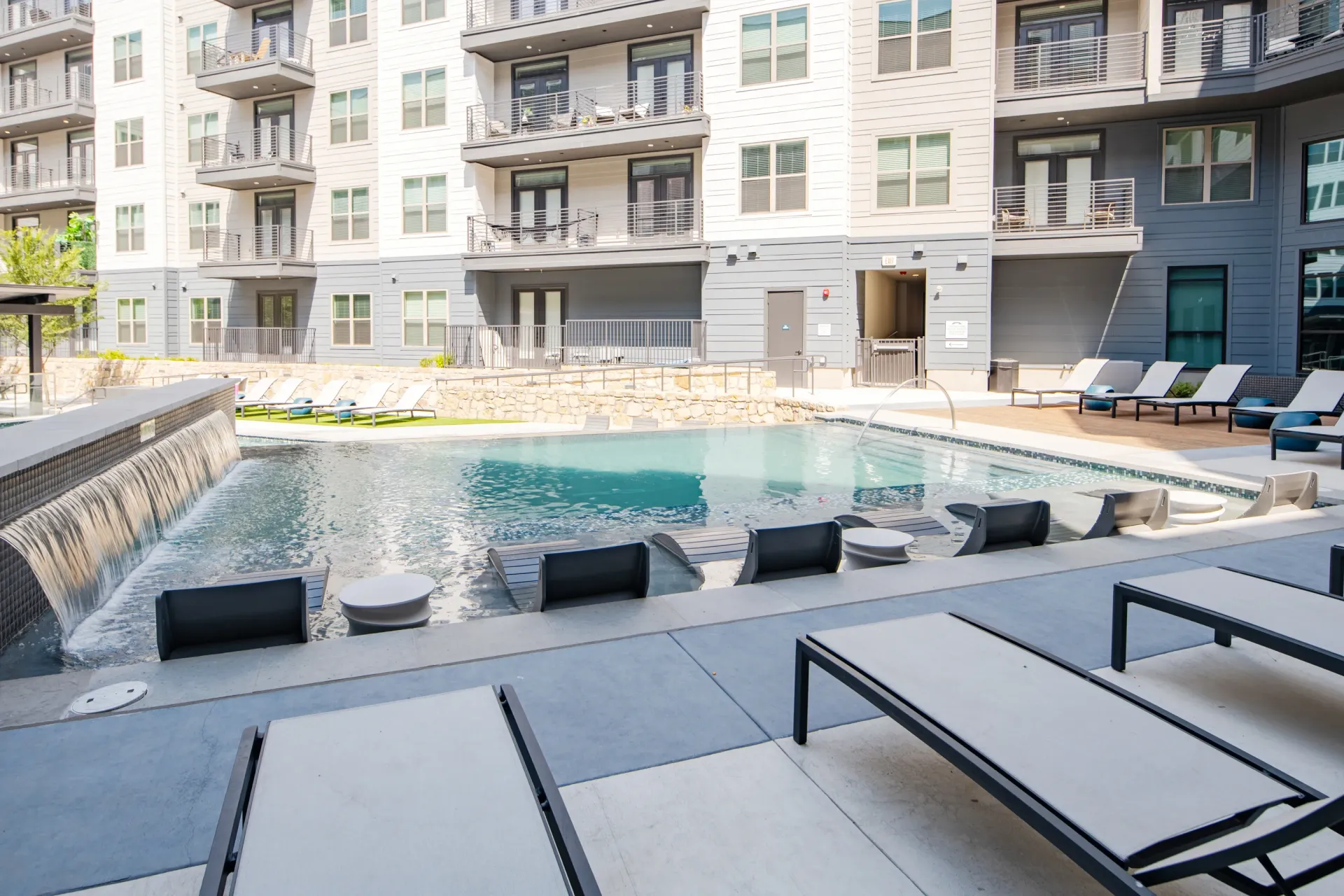 Swimming pool with lounge chairs and a waterfall feature at a modern apartment complex.