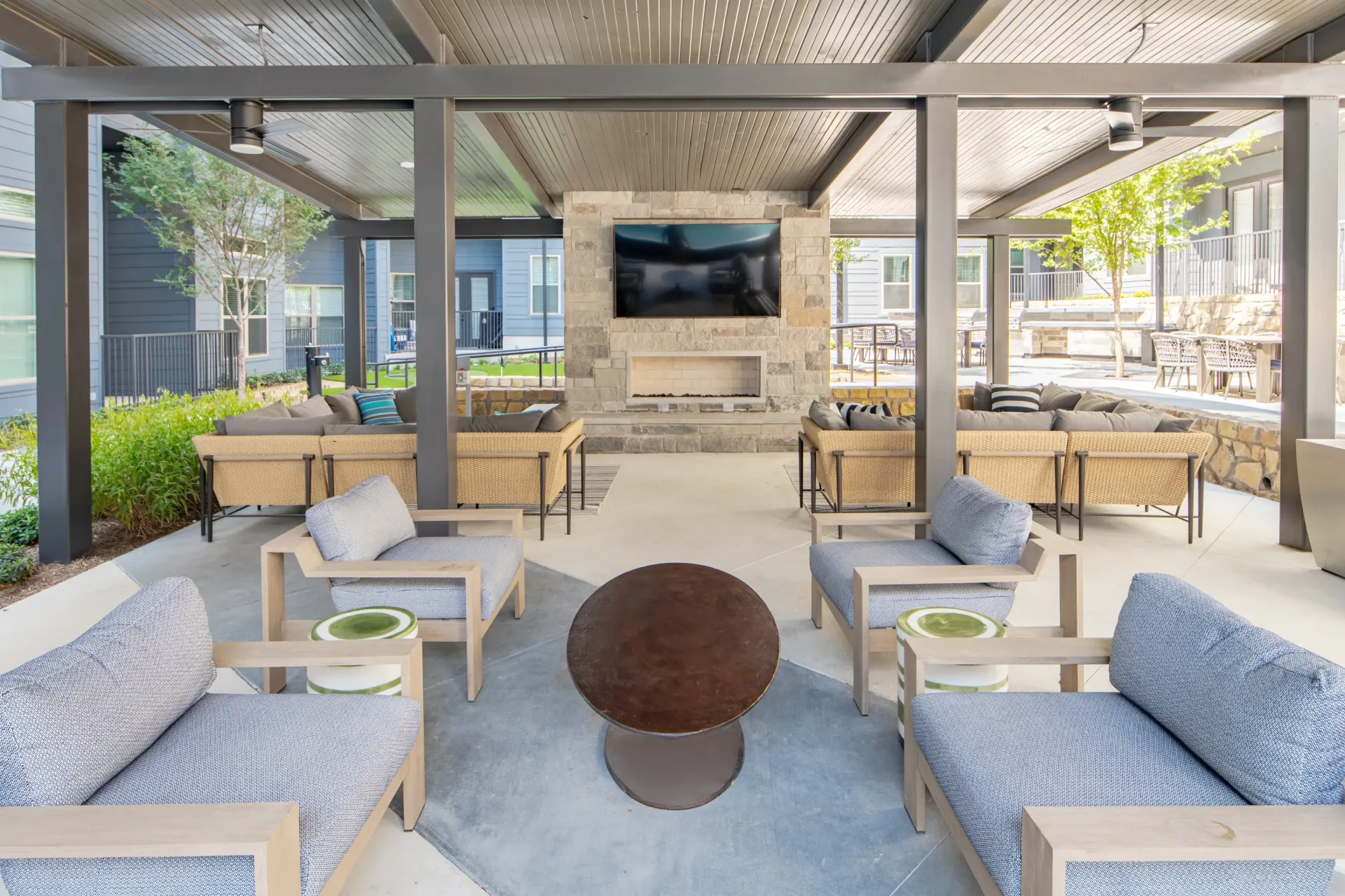 Outdoor covered lounge area with sectional sofas, chairs, a TV, and a fireplace.