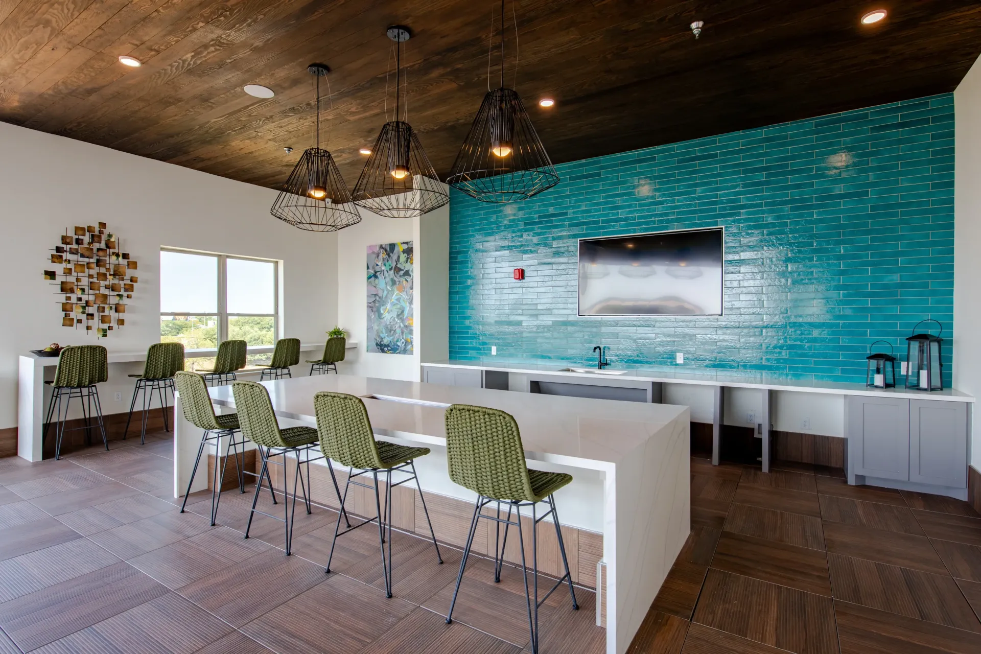 Modern communal lounge area with a long bar, green chairs, and a teal tiled accent wall with a TV.