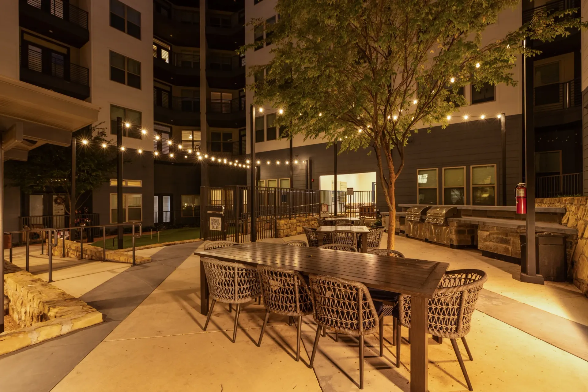 Outdoor dining area with tables, chairs, and grills lit by string lights at night.