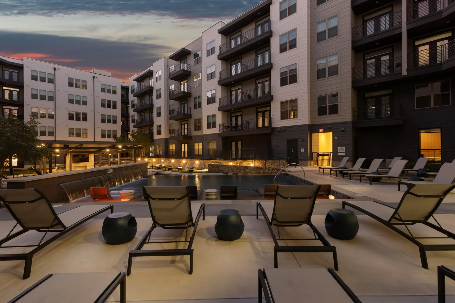 Modern apartment complex with a swimming pool and lounge chairs at dusk.