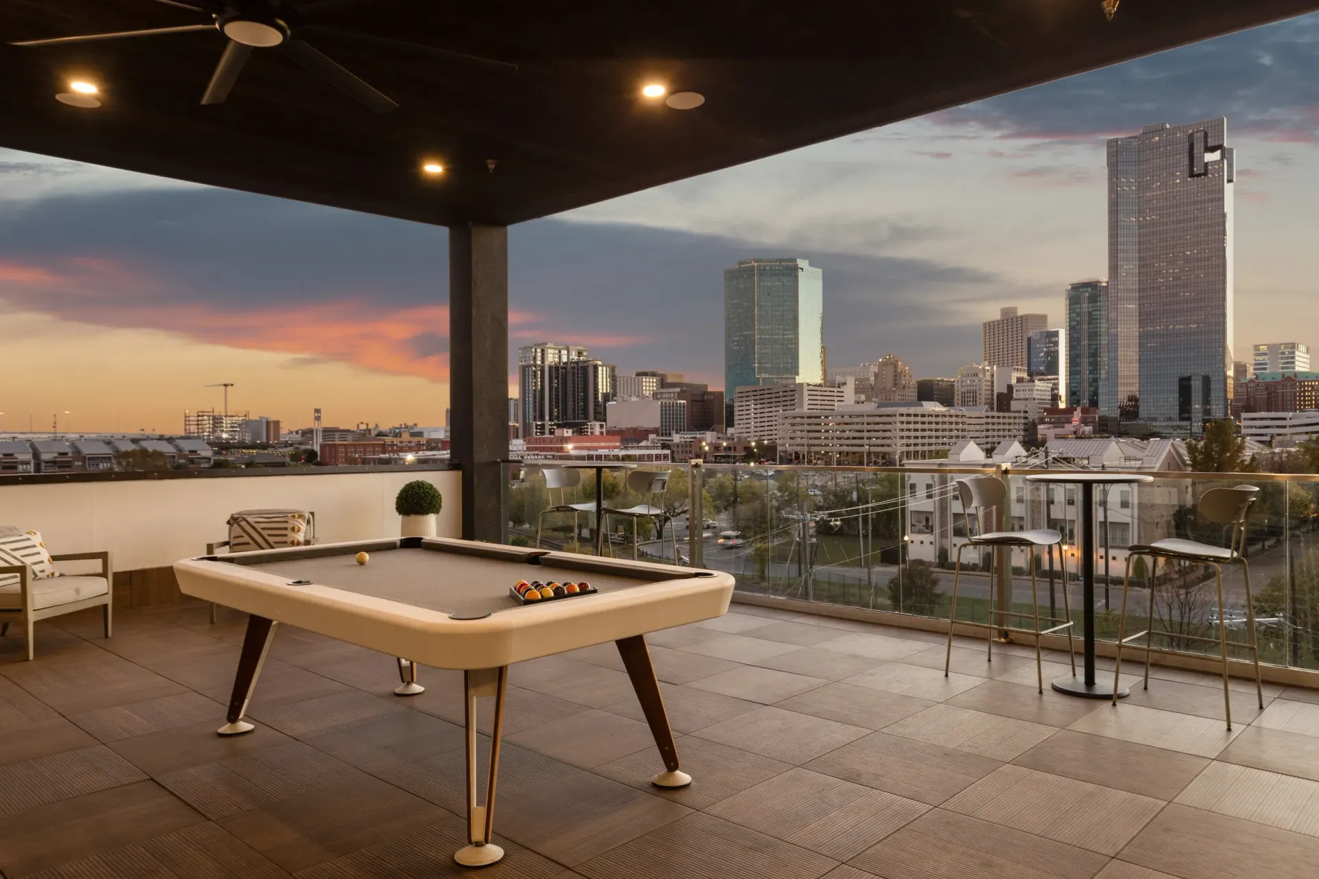 Rooftop patio with pool table and city skyline view at sunset.