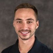 A young man with a beard and mustache is smiling for the camera.
