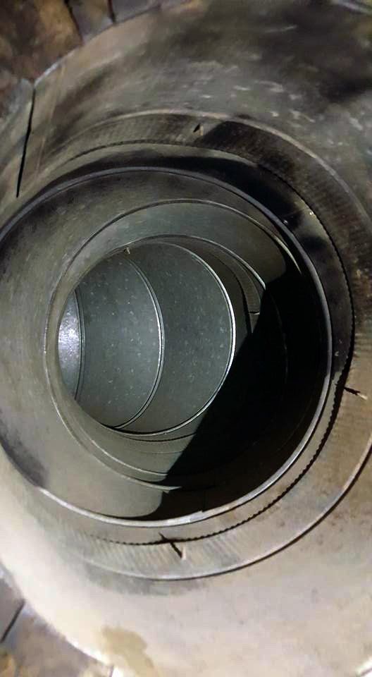 Inside view of a dirty, metal furnace vent with concentric circular walls.