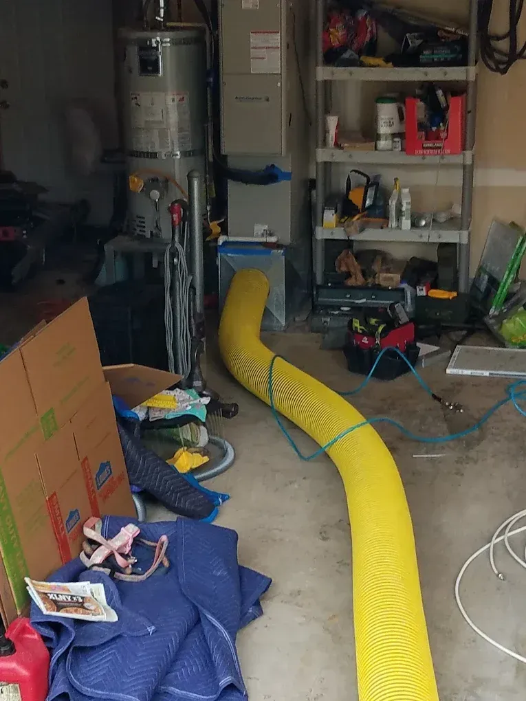 Cluttered garage with a yellow hose, water heater, shelving, and various items.