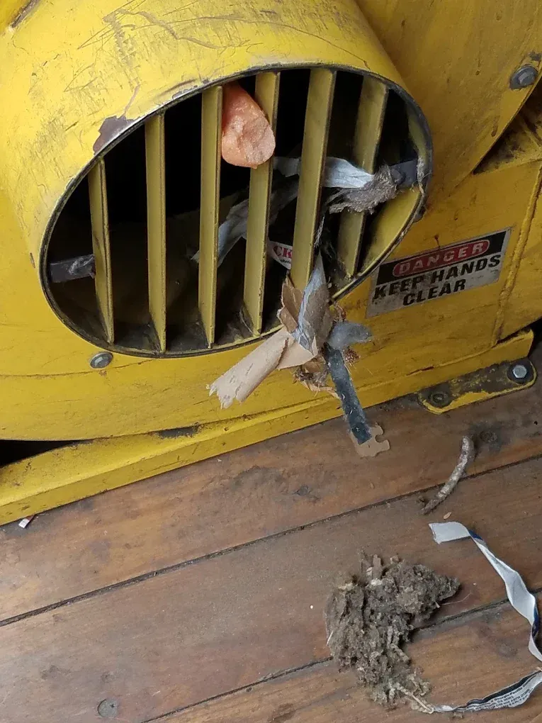 Yellow wood chipper with debris visible, wood floor. Safety warning label.