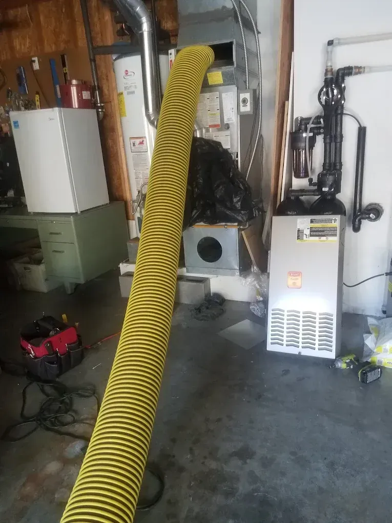 Yellow flexible ducting connected to HVAC system in a garage. Other equipment and tools visible.