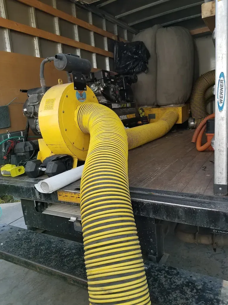 Yellow and black blower with a flexible hose, on the back of a truck.