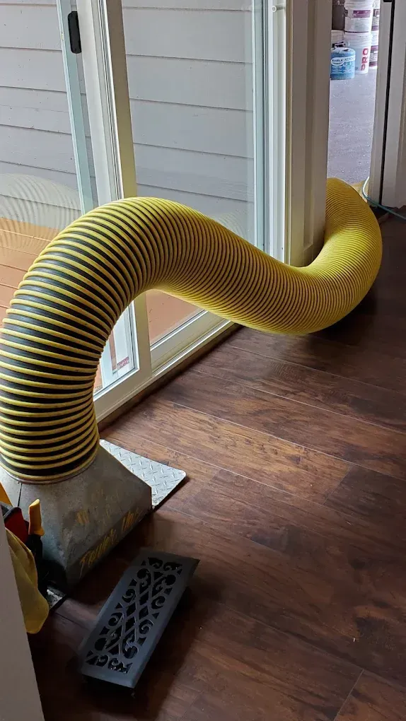 Yellow and black flexible hose running from inside, through a doorway, to outside. Wooden floor.
