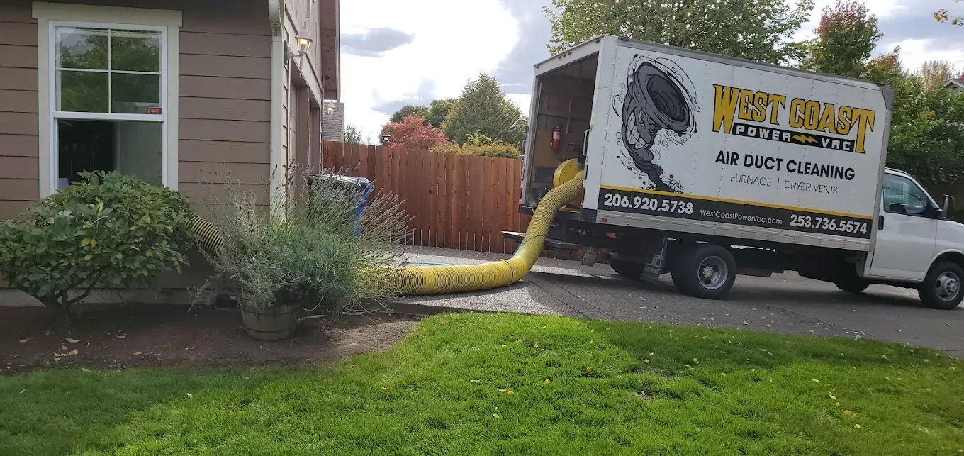 A truck with a yellow hose cleans air ducts near a house.
