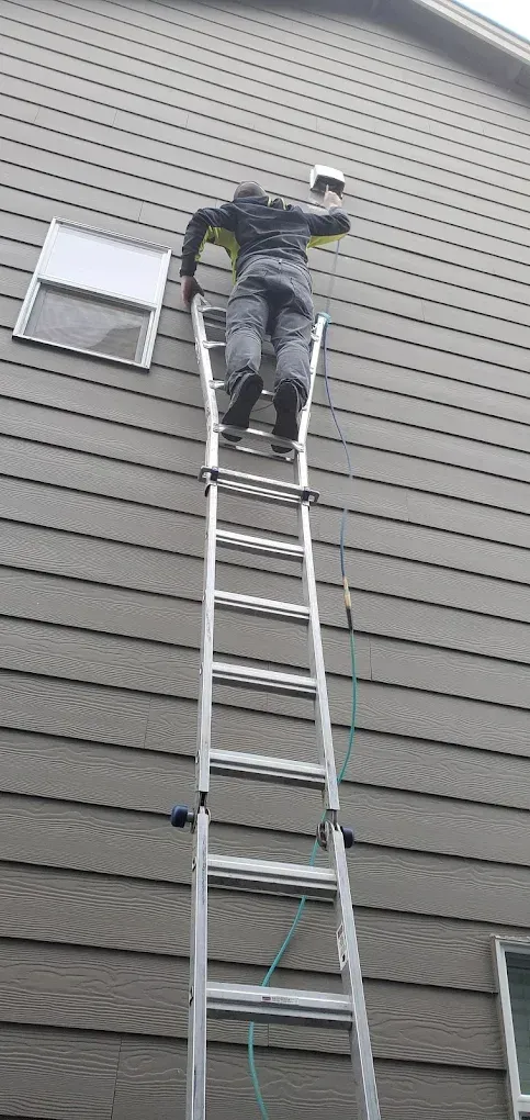 Person on a tall ladder painting the exterior of a house.