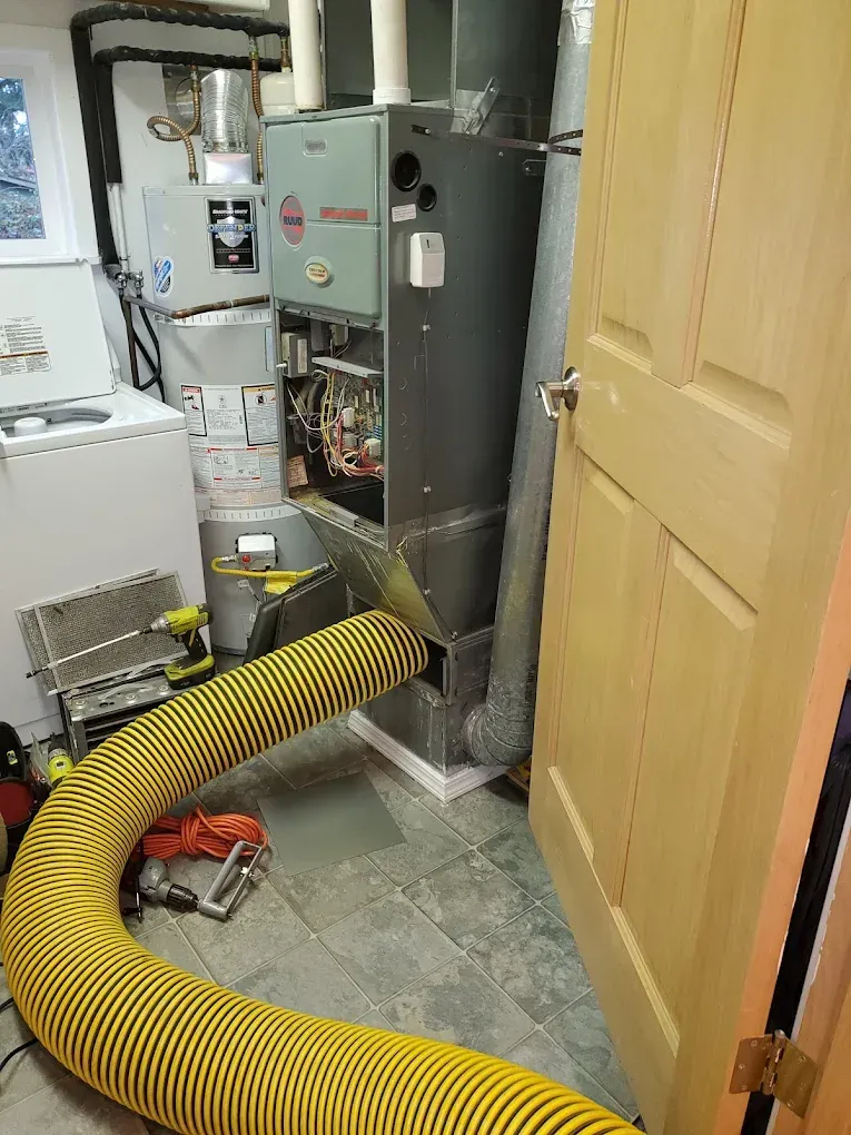 Furnace in a basement room with yellow hose; ajar wooden door on the right.