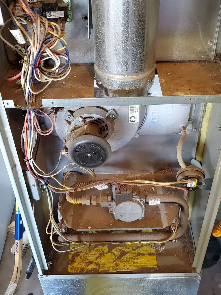 Furnace interior with blower, gas valve, and wiring, set in a dusty metal cabinet.