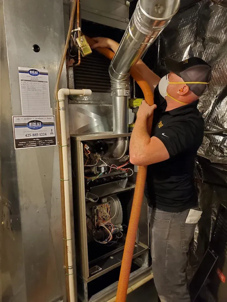 HVAC technician in a mask cleaning a furnace with a hose in a basement.