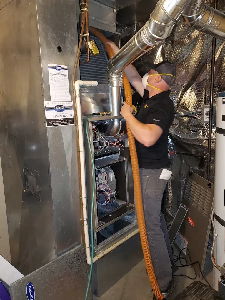 HVAC technician cleaning an air handler. Indoors, wearing a mask and using a vacuum hose.