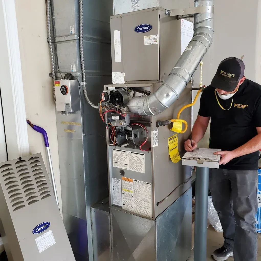 HVAC technician in mask, inspecting a Carrier furnace in a utility room.