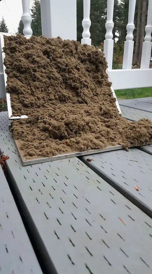 A tray of brown mulch on a gray deck, leaning against a white railing outdoors.