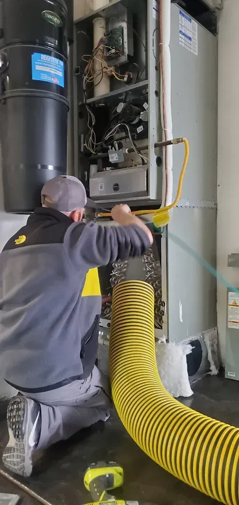 A person servicing a furnace, using a yellow hose.