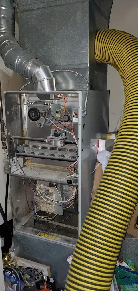 A furnace with its cover off, showing internal components, with a flexible yellow exhaust hose.