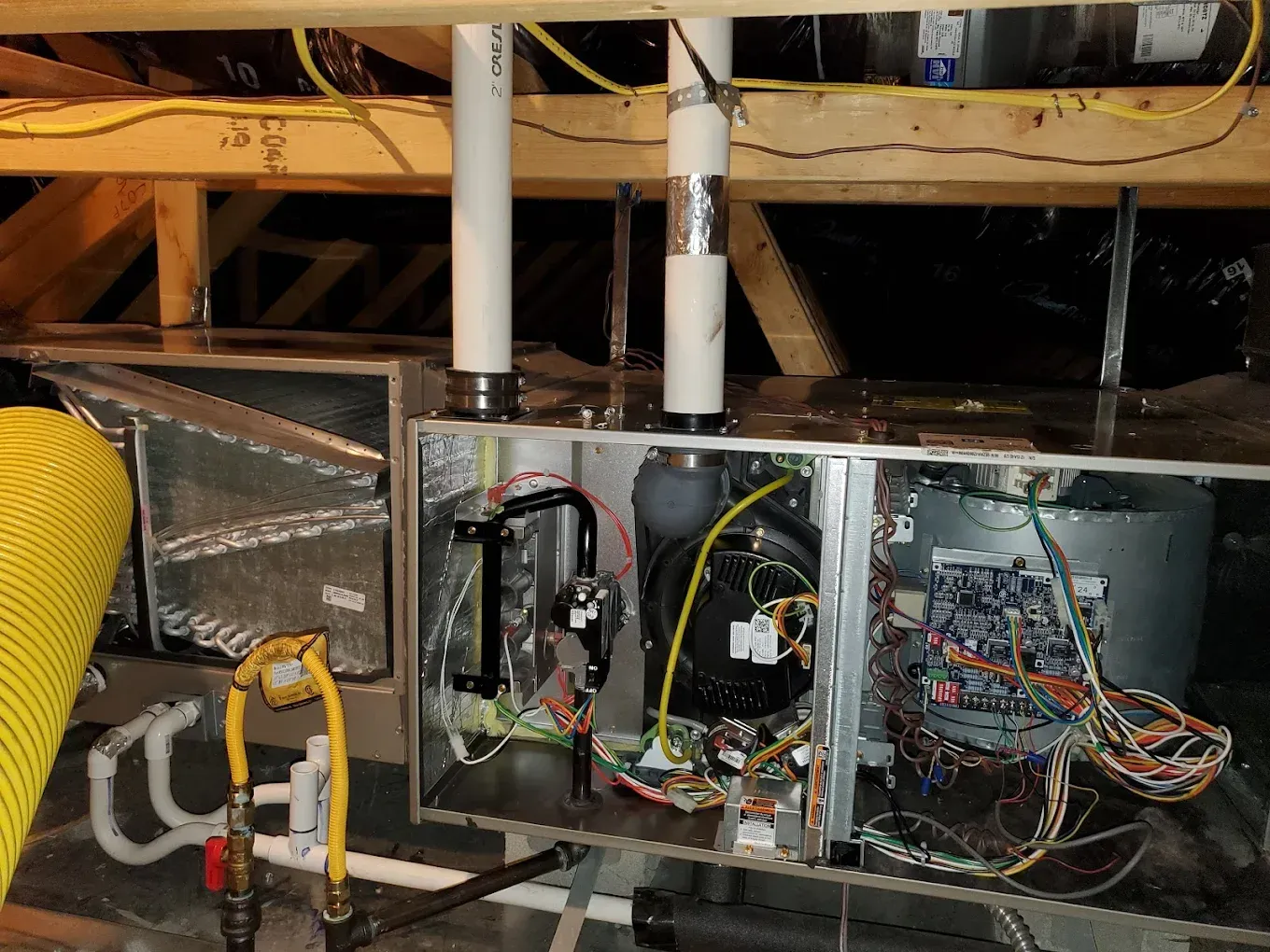 HVAC unit in an attic with ductwork, wiring, and pipes.