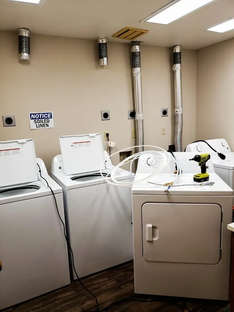 Laundry room with washing machines and dryers; air vents installed. A person is assembling a dryer.