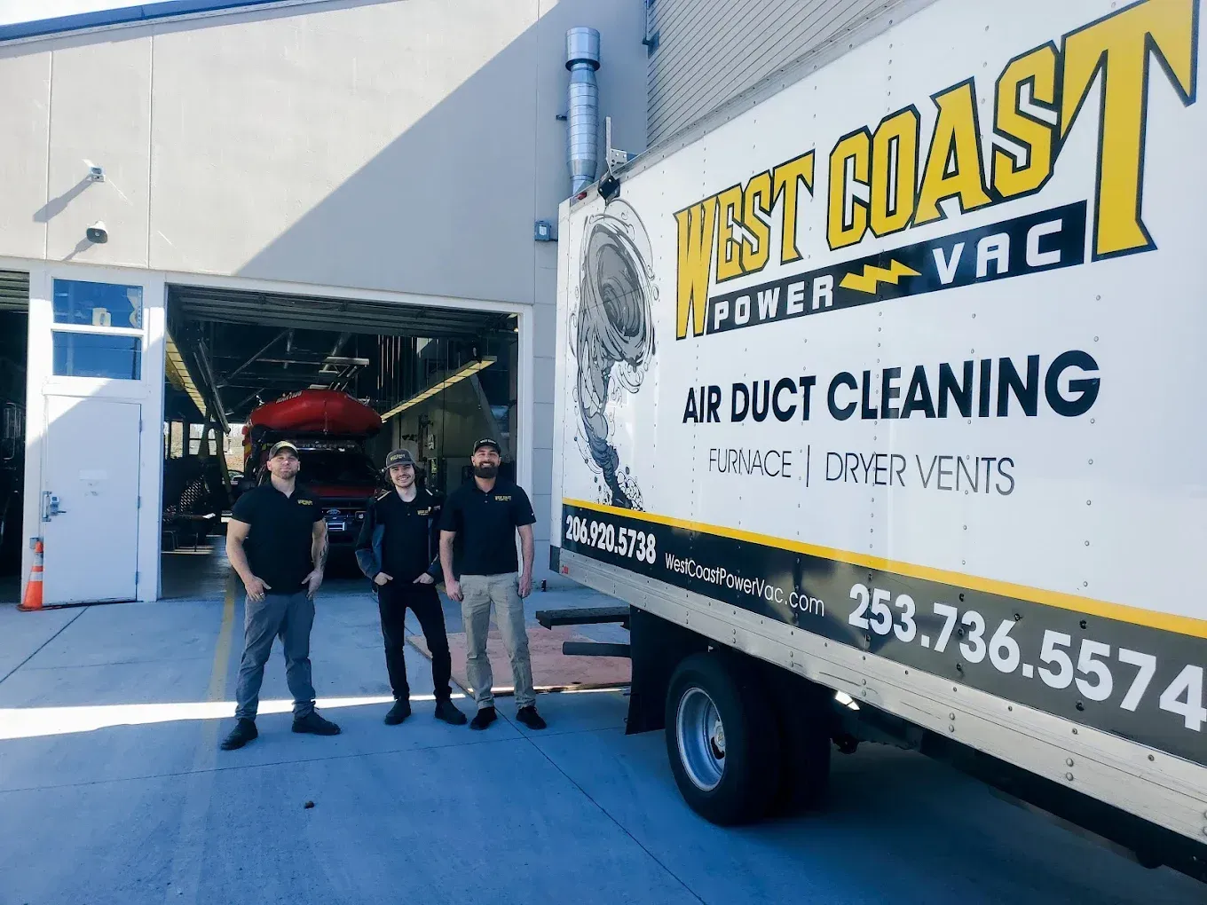 Three men stand beside a West Coast Power Vac truck, in front of a garage.