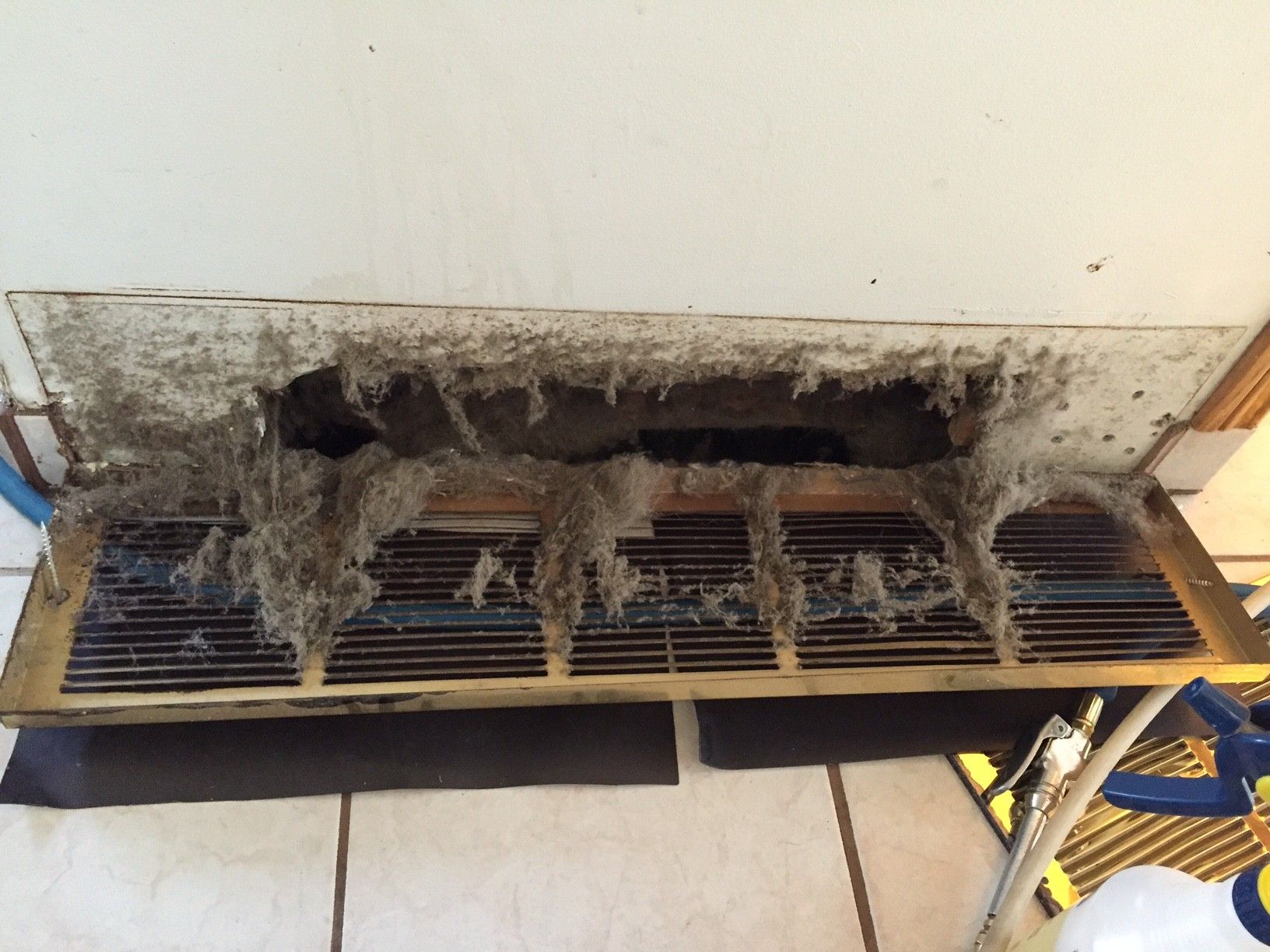 Dirty air vent covered in thick layers of dust and debris, attached to a white ceiling.