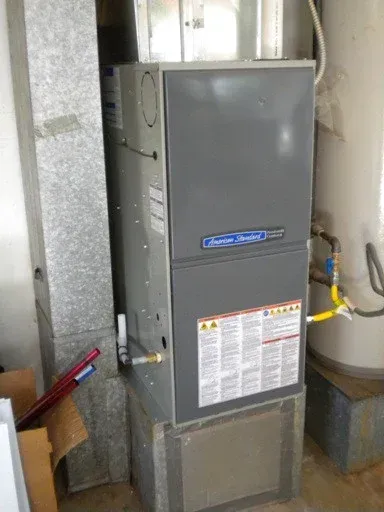 A gray furnace and ductwork in a utility room next to a water heater.