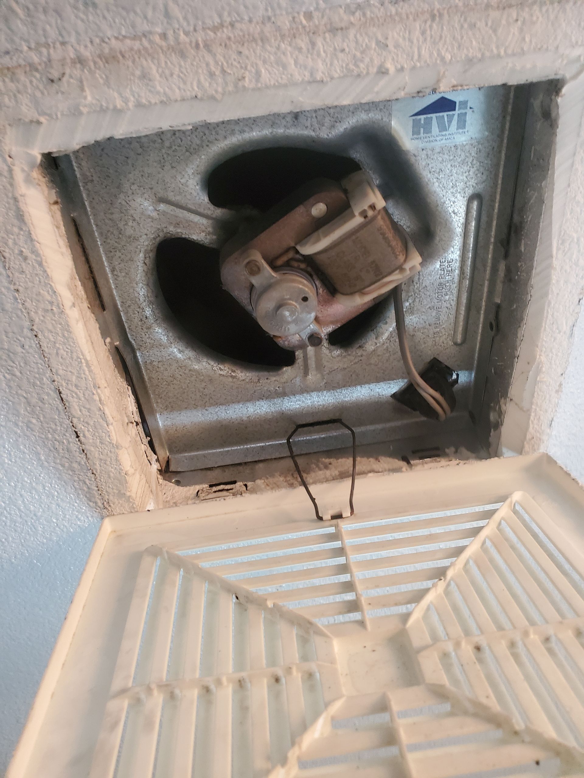 An open, frost-covered freezer revealing the fan motor and internal components, with a white plastic grill below.
