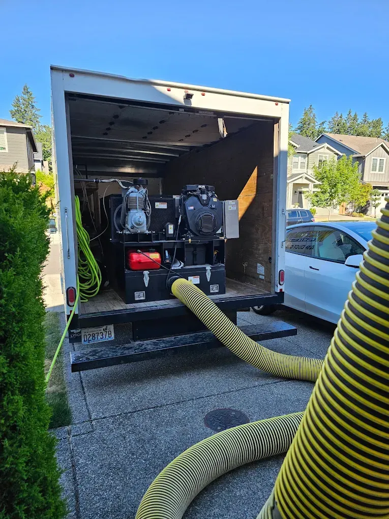 Truck bed open, containing industrial equipment; yellow hoses extend outward onto driveway.