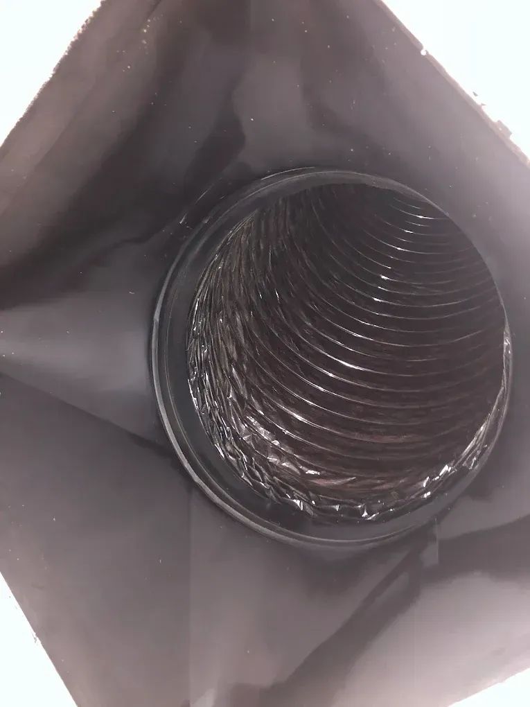 View inside a black flexible duct. The interior of the duct is metallic and wavy.