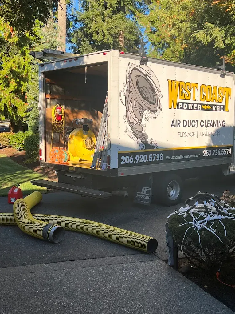 Air duct cleaning truck parked in a driveway with yellow hoses and equipment.