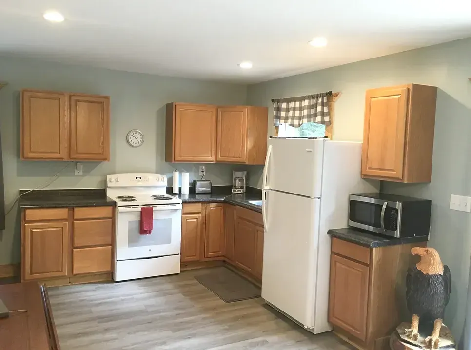 A kitchen with wooden cabinets, a white stove, a white refrigerator, a black microwave, and wood-patterned flooring.