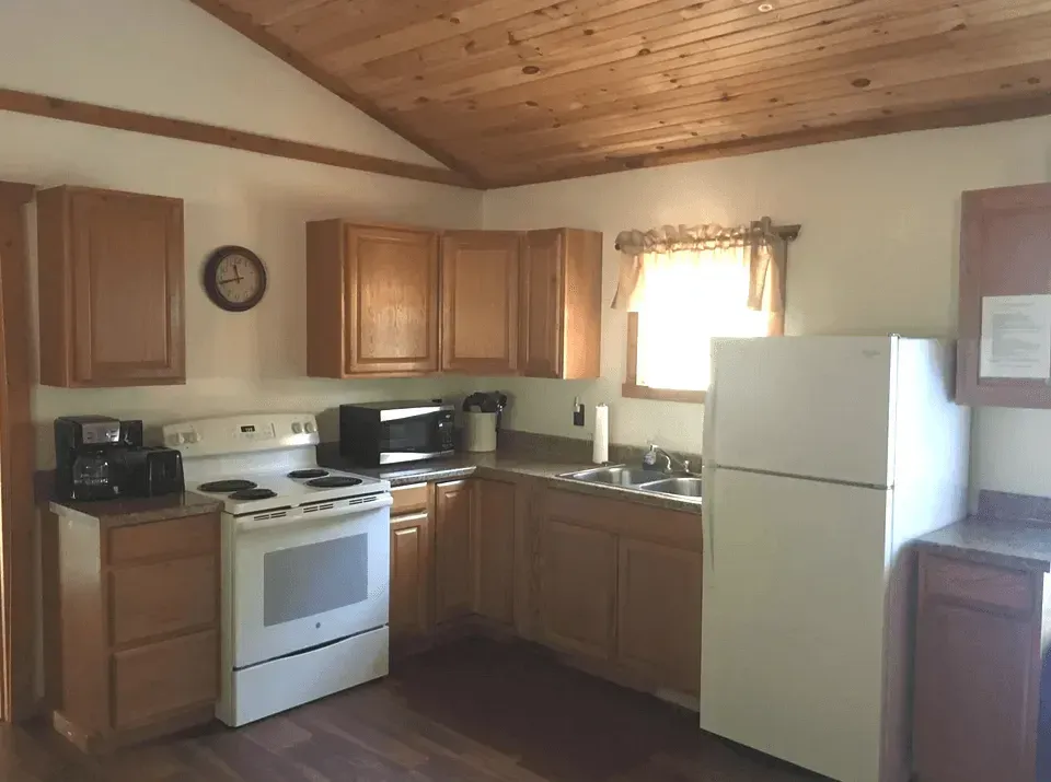 Modern kitchen with cream cabinets, a black range hood, marble island, and two wooden chairs in the foreground.