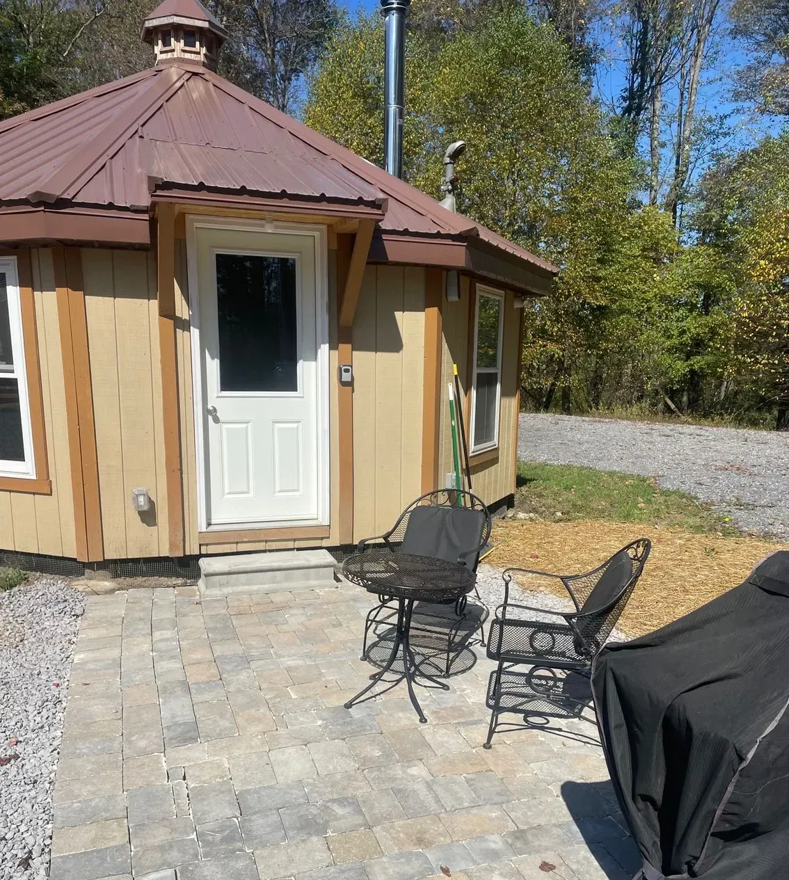 A tan yurt with a brown roof, white door, and patio area featuring a small metal table and two chairs.