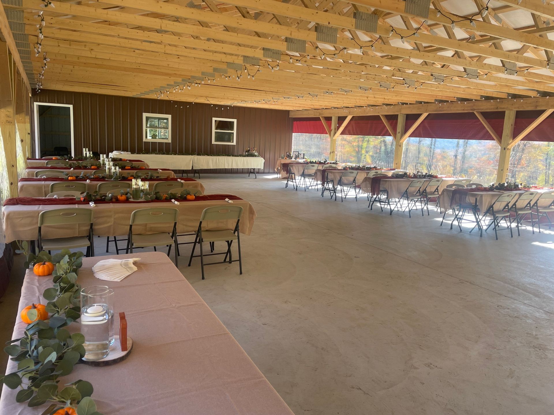 Wide rustic hall with rows of tables and chairs set up for an event, sunlight through open side walls