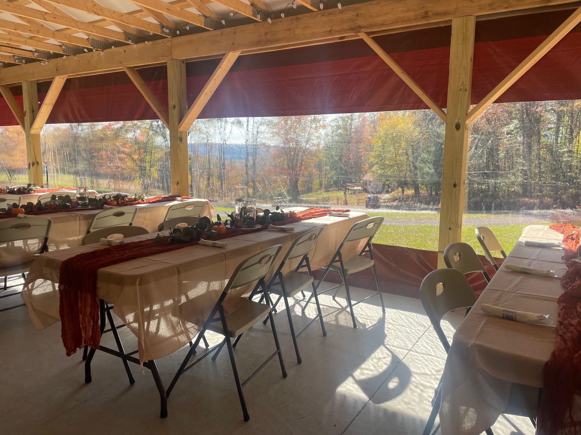 Covered outdoor banquet tables with white chairs and red table runners overlooking a sunny autumn lawn