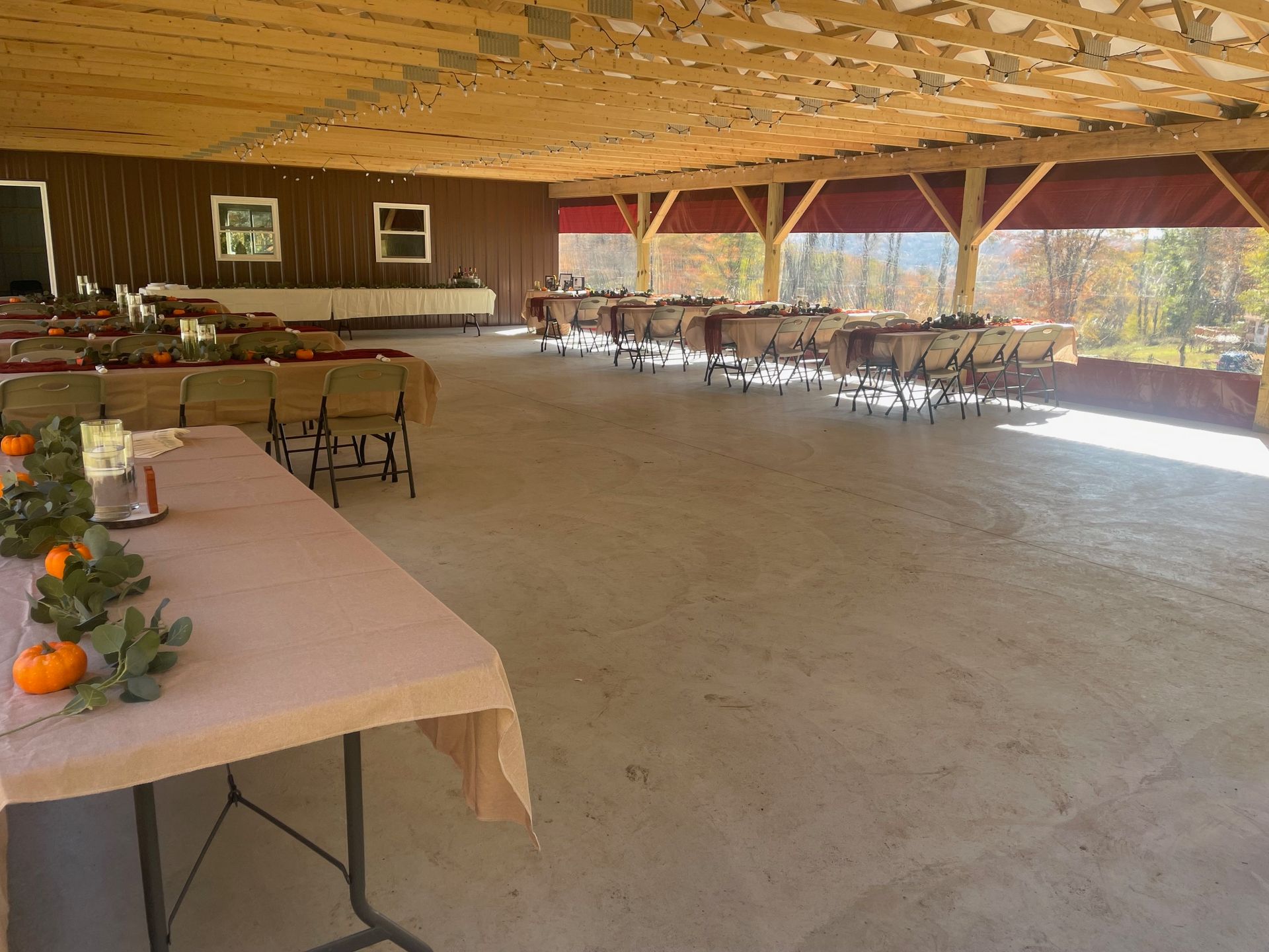 Open-sided pavilion with tables, chairs, and autumn decorations on a concrete floor