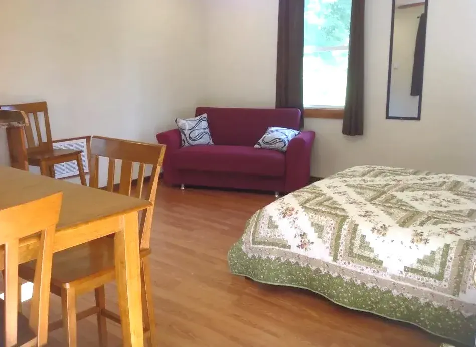Cozy bedroom-living room with wooden table, red sofa, and bed near a window