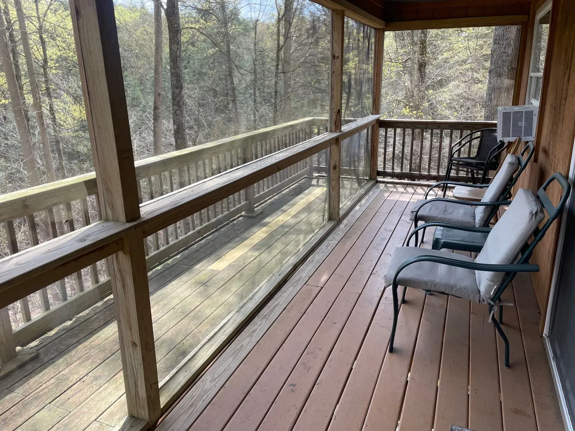 A screened-in porch with a blue sofa, wicker coffee table, and a small dining set overlooking green trees.