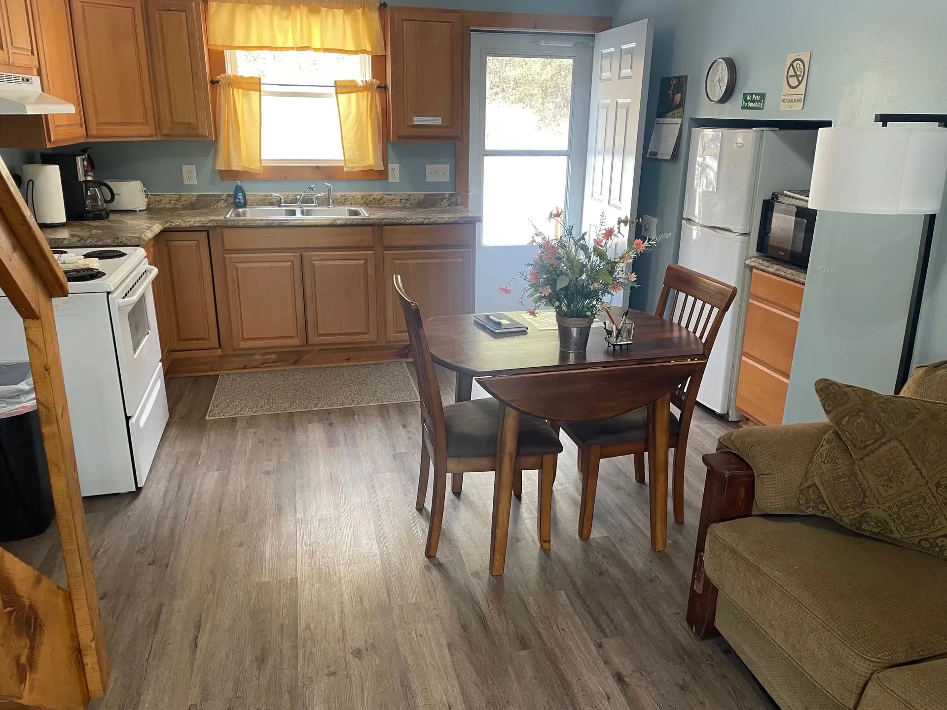 A kitchen with wood cabinets, light-colored flooring, a small dining table with chairs, and a white refrigerator.