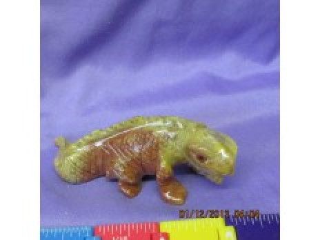 Small green-brown animal figurine on purple fabric beside a red ruler for scale