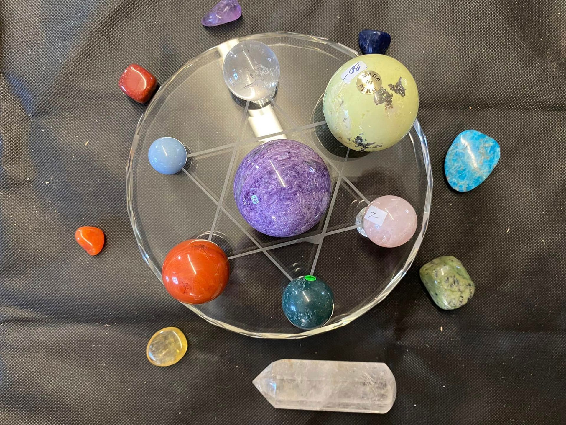 Crystal-covered display with a decorated book, wand, ankh, candles, and assorted gemstones on a reflective table