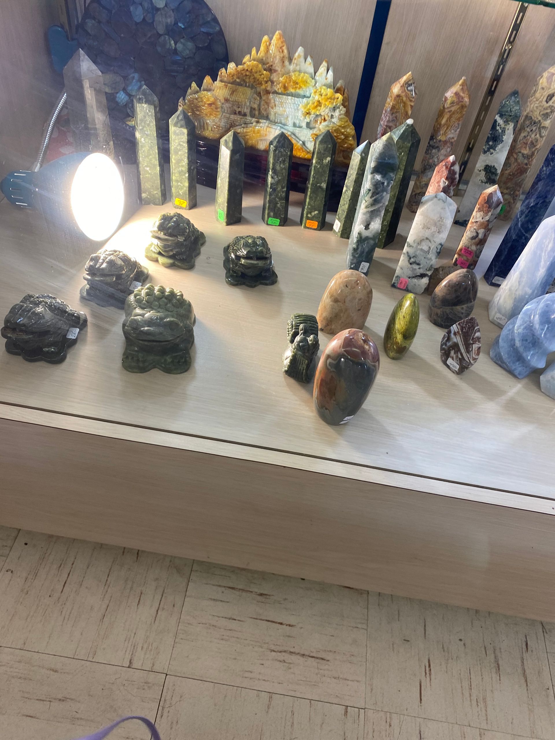 Crystal and mineral display on a shelf, with colorful polished stones and tall crystal towers lit by a lamp.